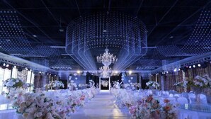 Un espacio con un pasillo central que conduce a un escenario, rodeado de mesas con centros de mesa florales.