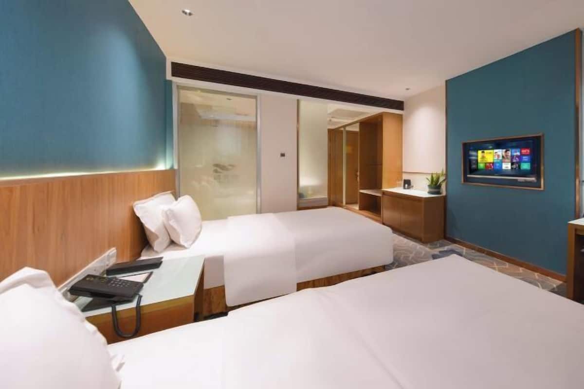 A hotel room with two beds, a desk with a phone, a TV on the wall, and a sliding door closet.