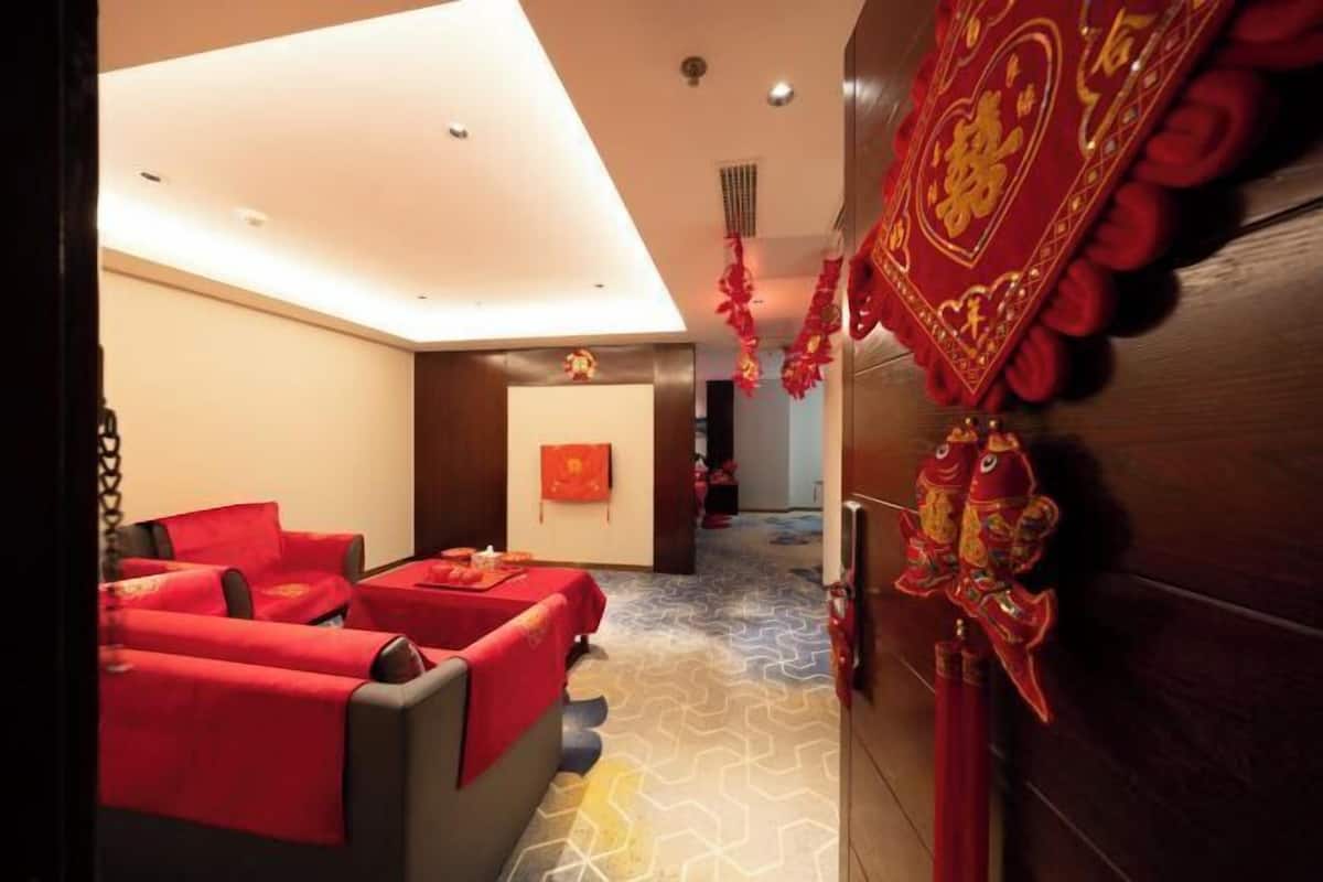 A hotel room with a modern design, featuring a sofa set and a small table with a red tablecloth.