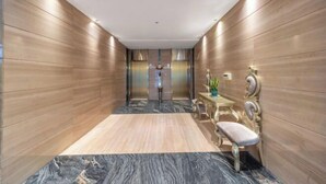 Un pasillo moderno con paneles de madera, suelo de mármol y un banco con una mesita y una planta.