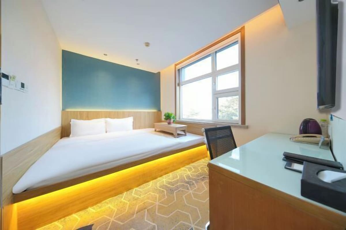 A modern hotel room with a bed, bedside table, and a desk area.