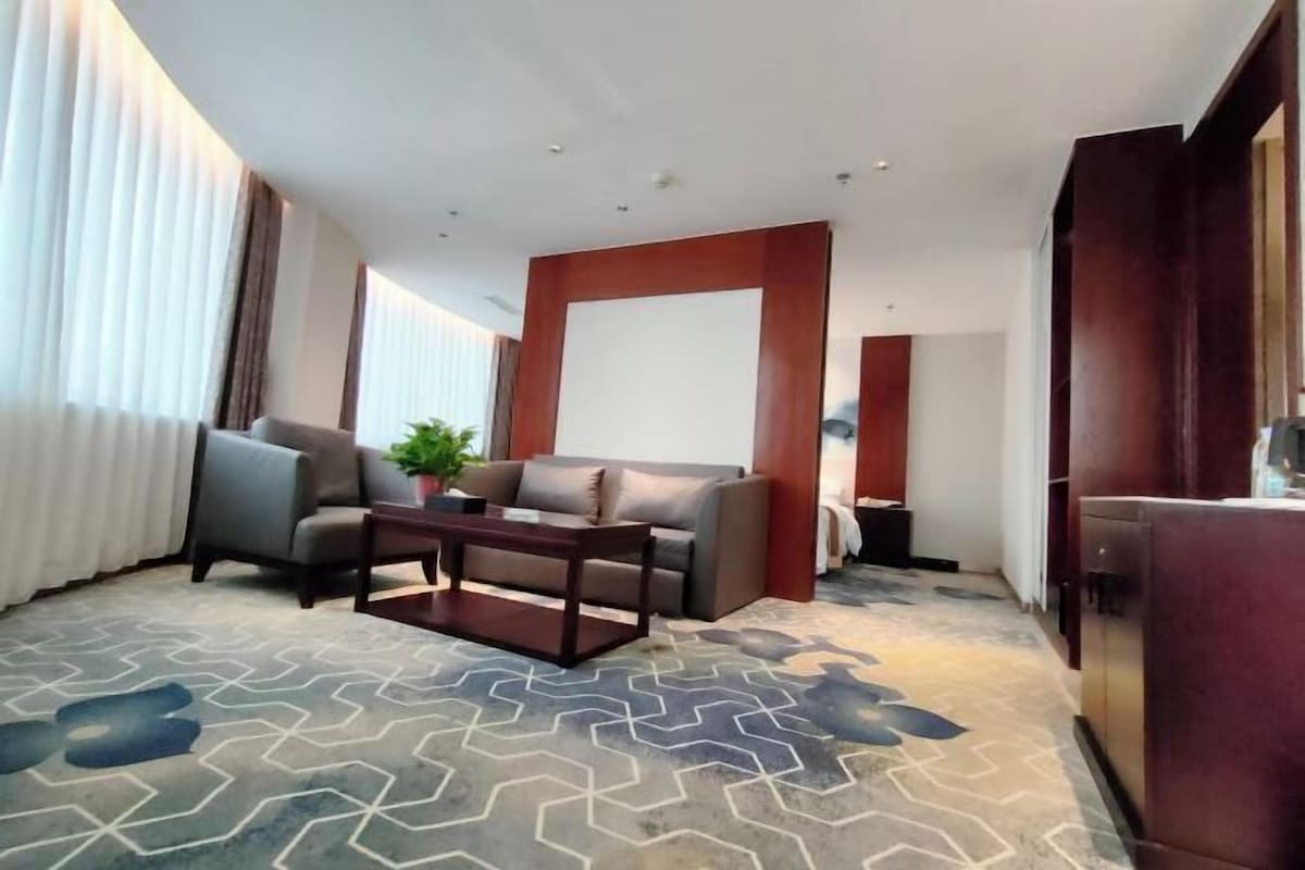 A modern hotel room with a grey sofa, a wooden coffee table, and a patterned carpet.
