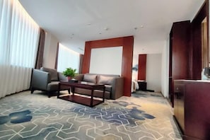A modern hotel room with a grey sofa, a wooden coffee table, and a patterned carpet.