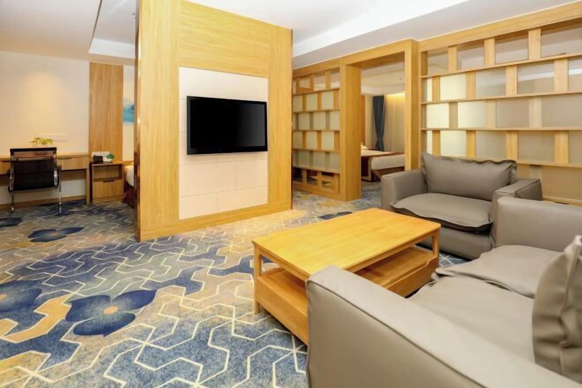 A modern living room with a sofa, a coffee table, a TV mounted on a wooden wall, and a patterned carpet.