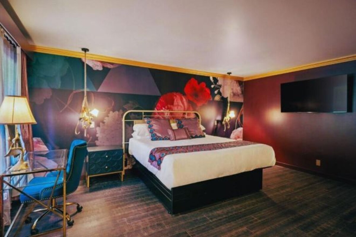 A bedroom with a bed, a desk, and a chair. There is a TV on the wall.