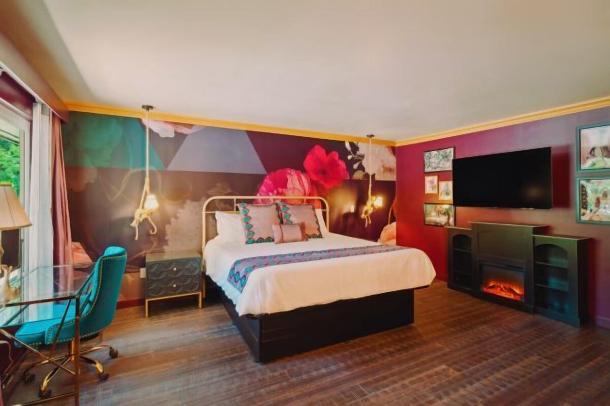 Un dormitorio con cama, escritorio, silla, televisor y chimenea.