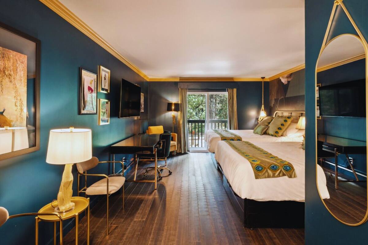 A hotel room with a bed, a desk, a chair, a lamp, and a large mirror.