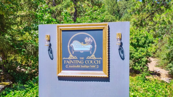 A framed sign for The Fainting Couch Maximallist Boutique Hotel, surrounded by lush greenery. - The Fainting Couch Boutique Hotel (Cobb)