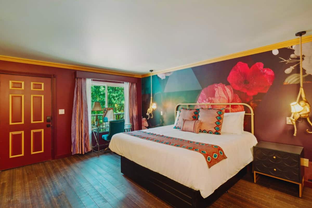 A bedroom with a large bed, a nightstand, a door with a unique design, and a mural on the wall.