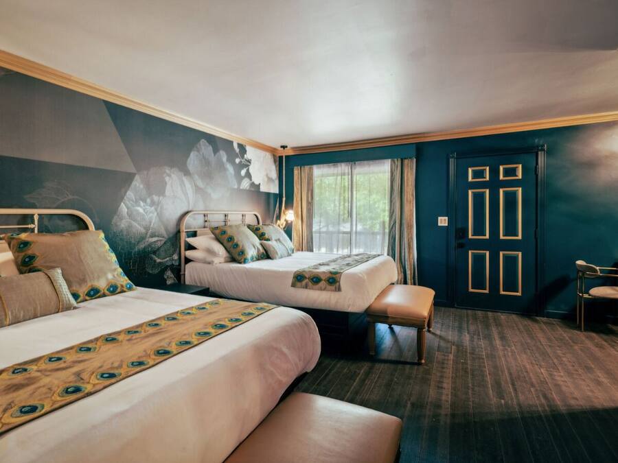 A hotel room with two beds, a bench, a door with a geometric design, and a wall mural.