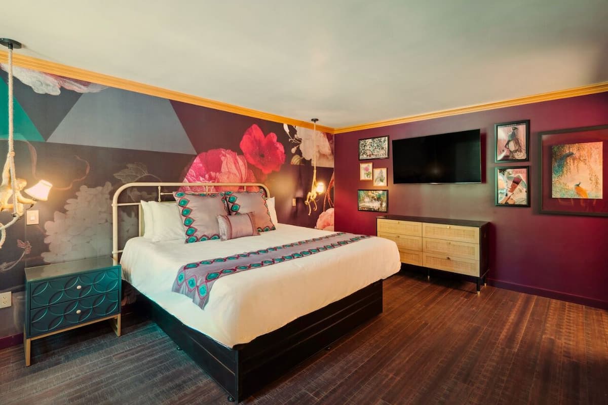 A modern bedroom with a large bed, a dresser, a TV, and artwork on the walls.