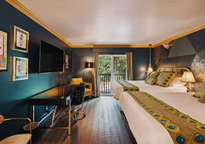 Quarto de hotel com cama, escrivaninha, cadeira, televisão e varanda com vista para árvores.