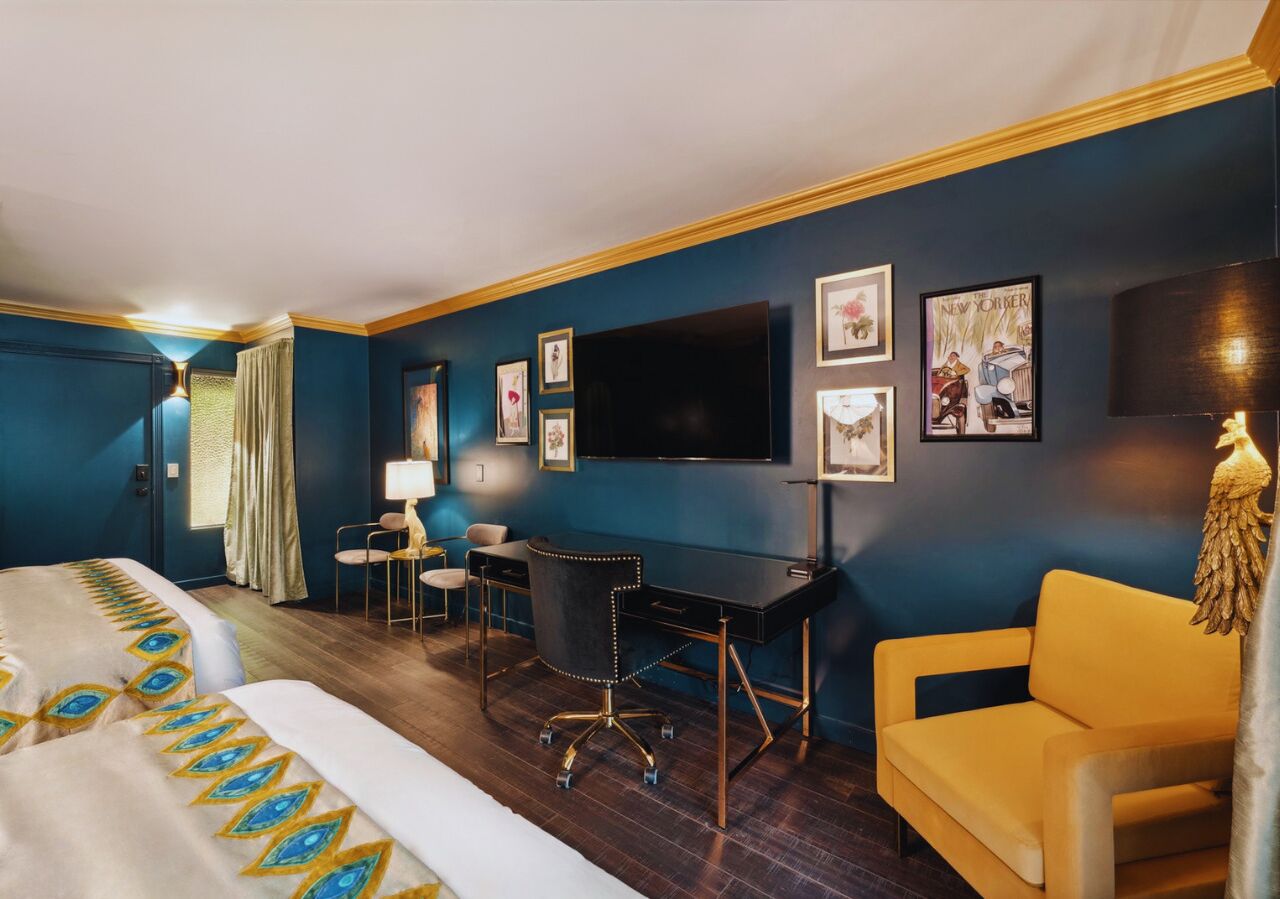 A hotel room with a bed, desk, chair, and a television on the wall.