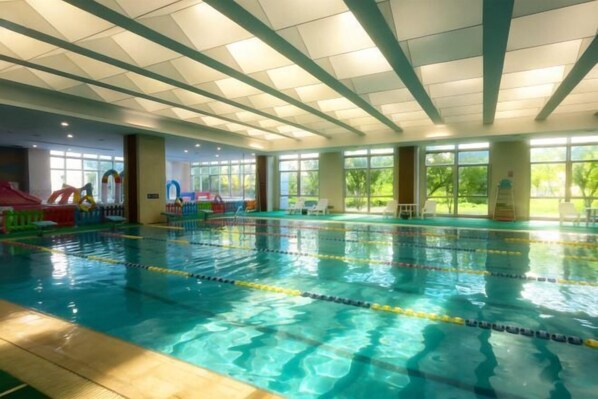 Uma piscina interior com pistas demarcadas, grandes janelas e área de recreação com equipamentos coloridos.