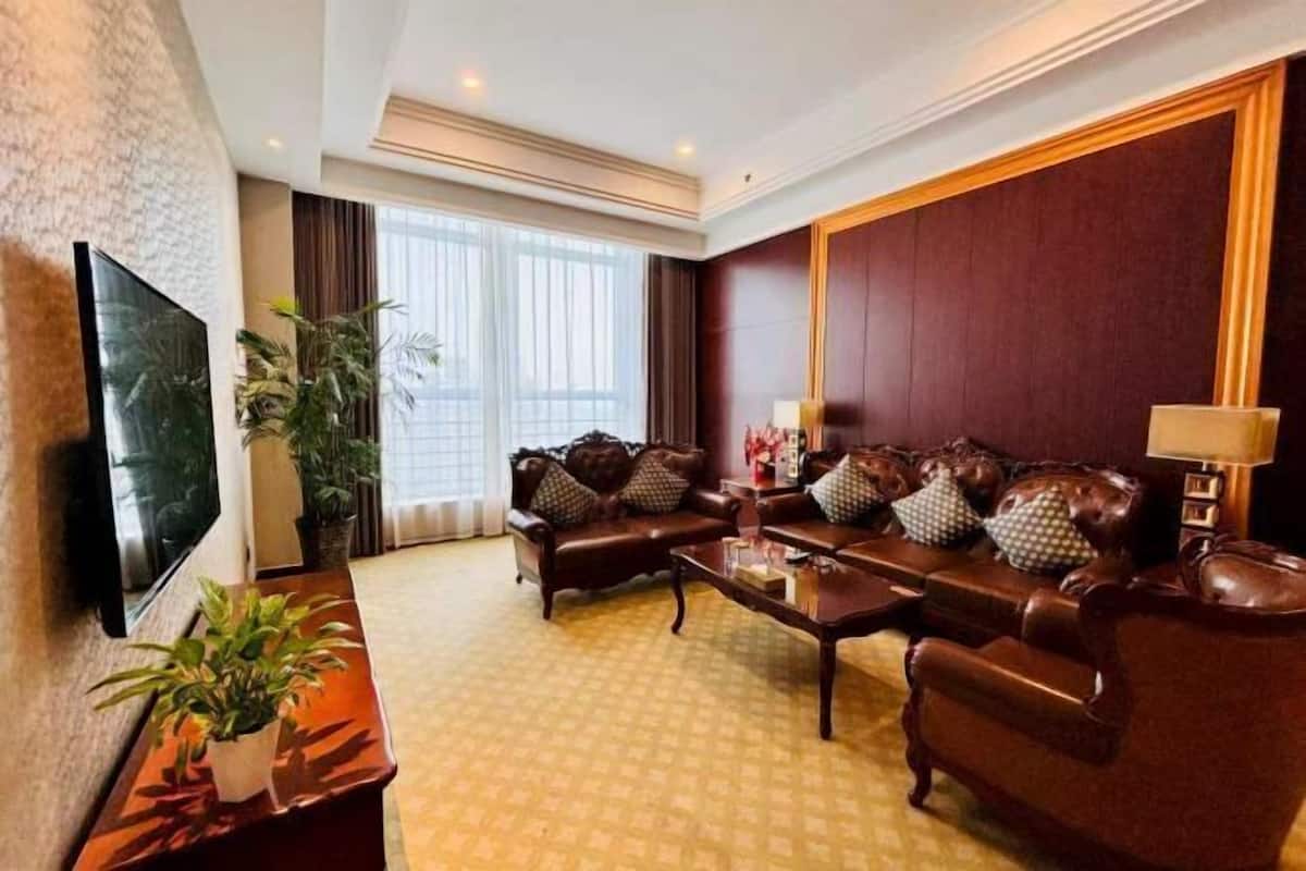 Ein Hotelzimmer mit einem großen Flachbildfernseher, zwei Ledersofas, einem Couchtisch und einer Zimmerpflanze.