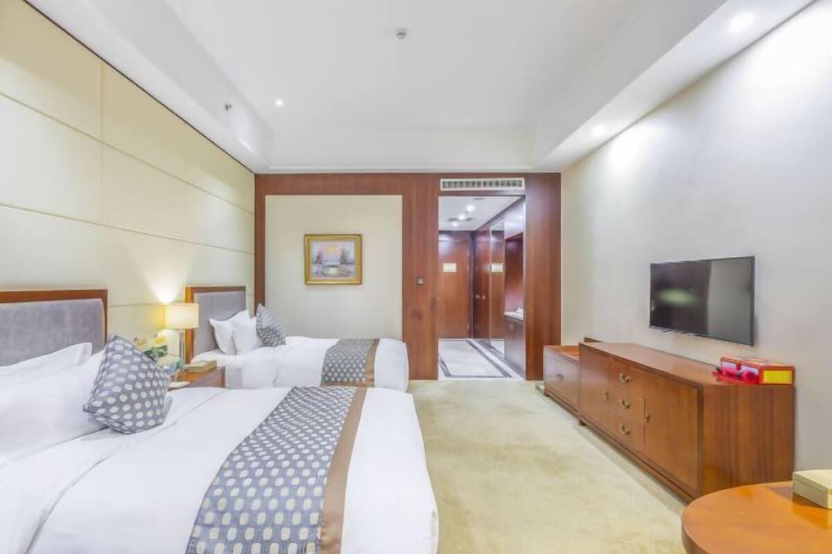 Ein Hotelzimmer mit zwei Betten, einem Fernseher, einer Holzkommode und einem Gemälde an der Wand.