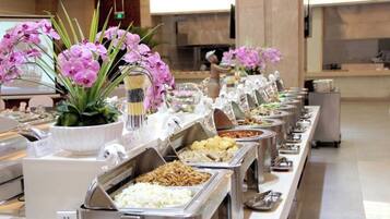 A buffet with various food options and decorative flowers.