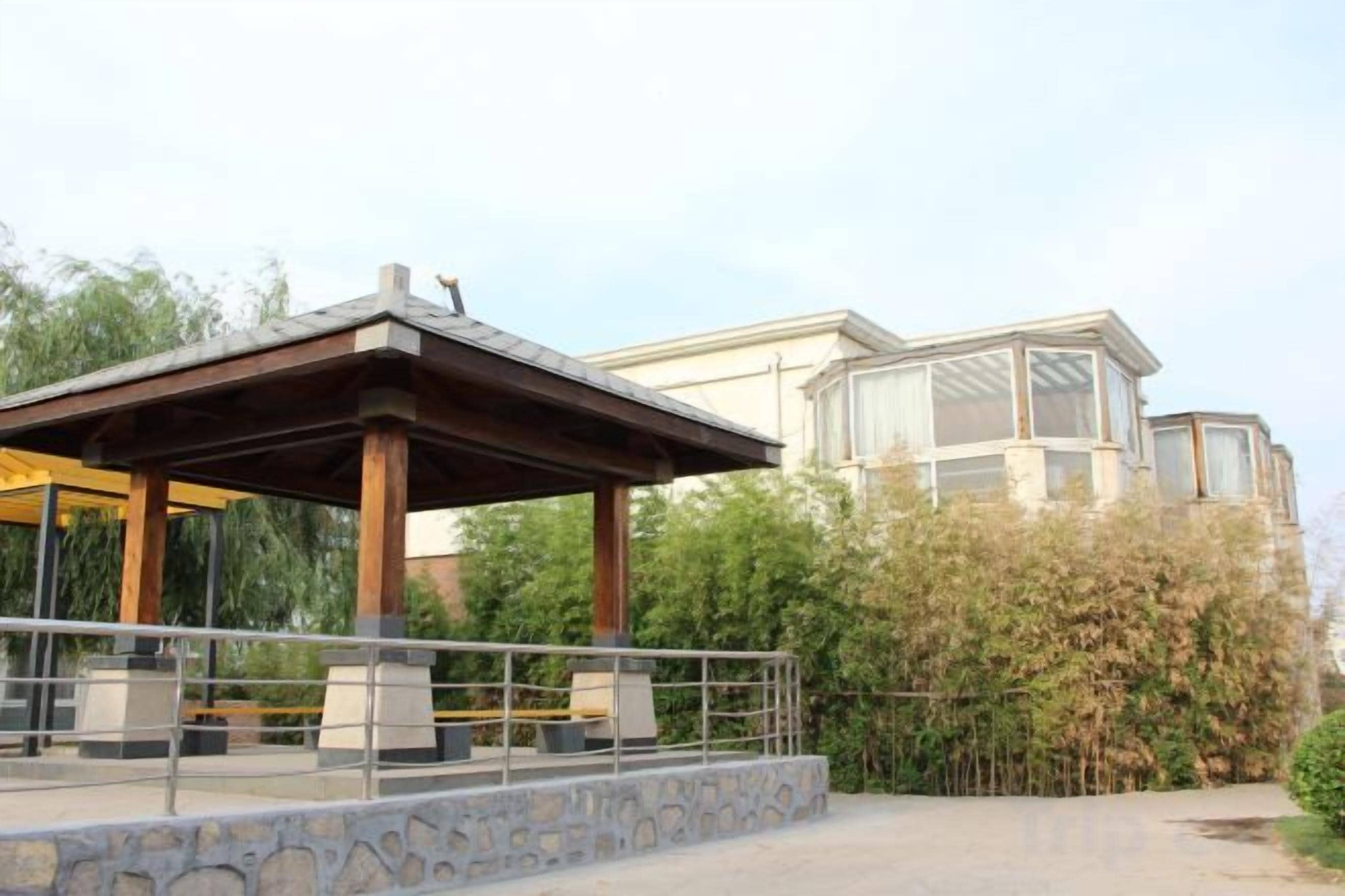 A covered outdoor seating area with stone steps leading up to it, a building with large windows in the background, and a clear sky.