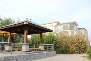 A covered outdoor seating area with stone steps leading up to it, a building with large windows in the background, and a clear sky. - Bohai International Hotel (Huanghua)