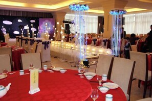 Een banketzaal met ronde tafels gedekt voor een diner, een podium met decor en een sierlijke verlichtingsarmatuur.