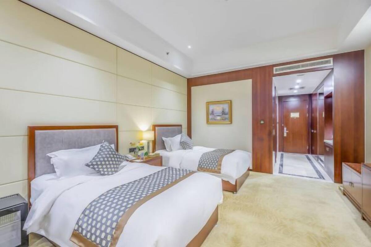 Ein Hotelzimmer mit zwei Betten, einem Holzkopfende, einem Nachttisch mit Lampe und einem gerahmten Bild an der Wand.