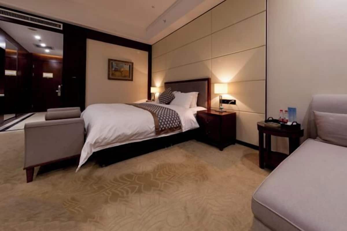 Ein Hotelzimmer mit einem großen Bett, einem Nachttisch mit Lampe, einem Sessel und einem Teppichboden.