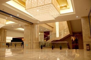 Un lobby espacioso con una gran lámpara de araña, pisos de mármol y una escalera que conduce a los niveles superiores.