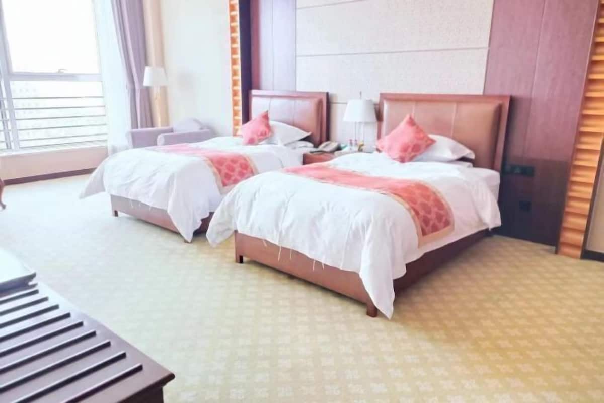 Ein Hotelzimmer mit zwei Betten, einem Schreibtisch und einem fensterbepflanzten Fenster.