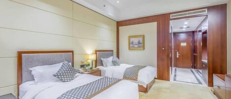 A hotel room with two beds, a wooden headboard, a nightstand, a lamp, and a framed picture on the wall.