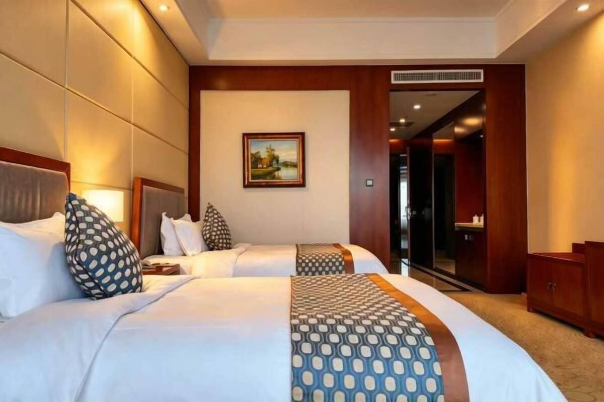 Ein Hotelzimmer mit zwei Betten, einem Bild an der Wand und Blick auf den Flur.