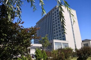 Un edificio alto y moderno con fachada de vidrio, rodeado de vegetación y un cielo azul despejado.
