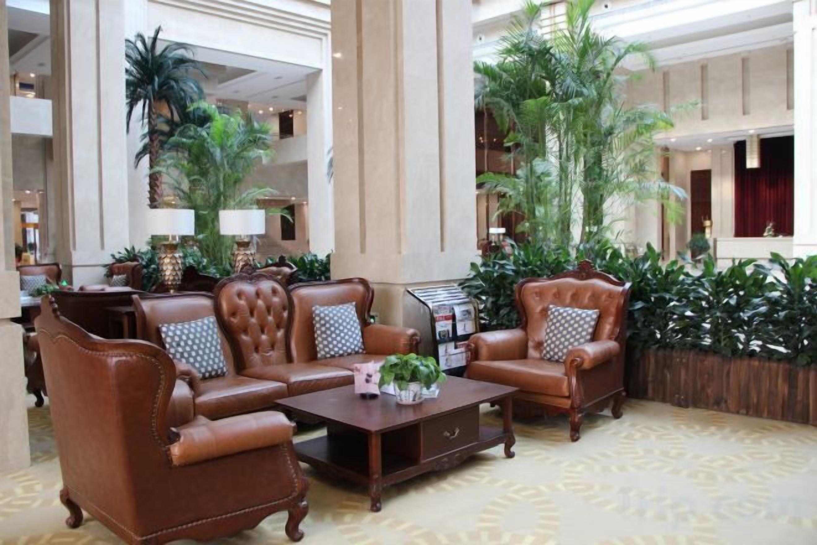 A lobby with a brown leather sofa set, a wooden coffee table, and a large potted plant.