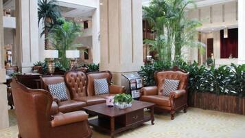 A lobby with a brown leather sofa set, a wooden coffee table, and a large potted plant.