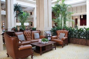 Un hall d’entrée avec un ensemble de canapés en cuir marron, une table basse en bois et une grande plante en pot.