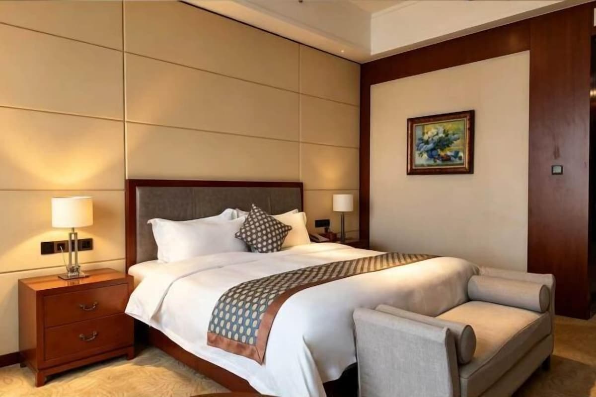 Una habitación de hotel con una cama grande, una mesita de noche, un sofá y un cuadro en la pared.