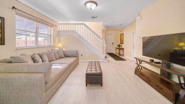 Amplia sala de estar con una televisión de pantalla plana grande, un sofá, una mesa de centro de vidrio y una escalera que conduce a otro nivel.