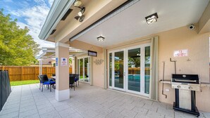 Un patio techado con una parrilla, asientos exteriores y vistas a una piscina.