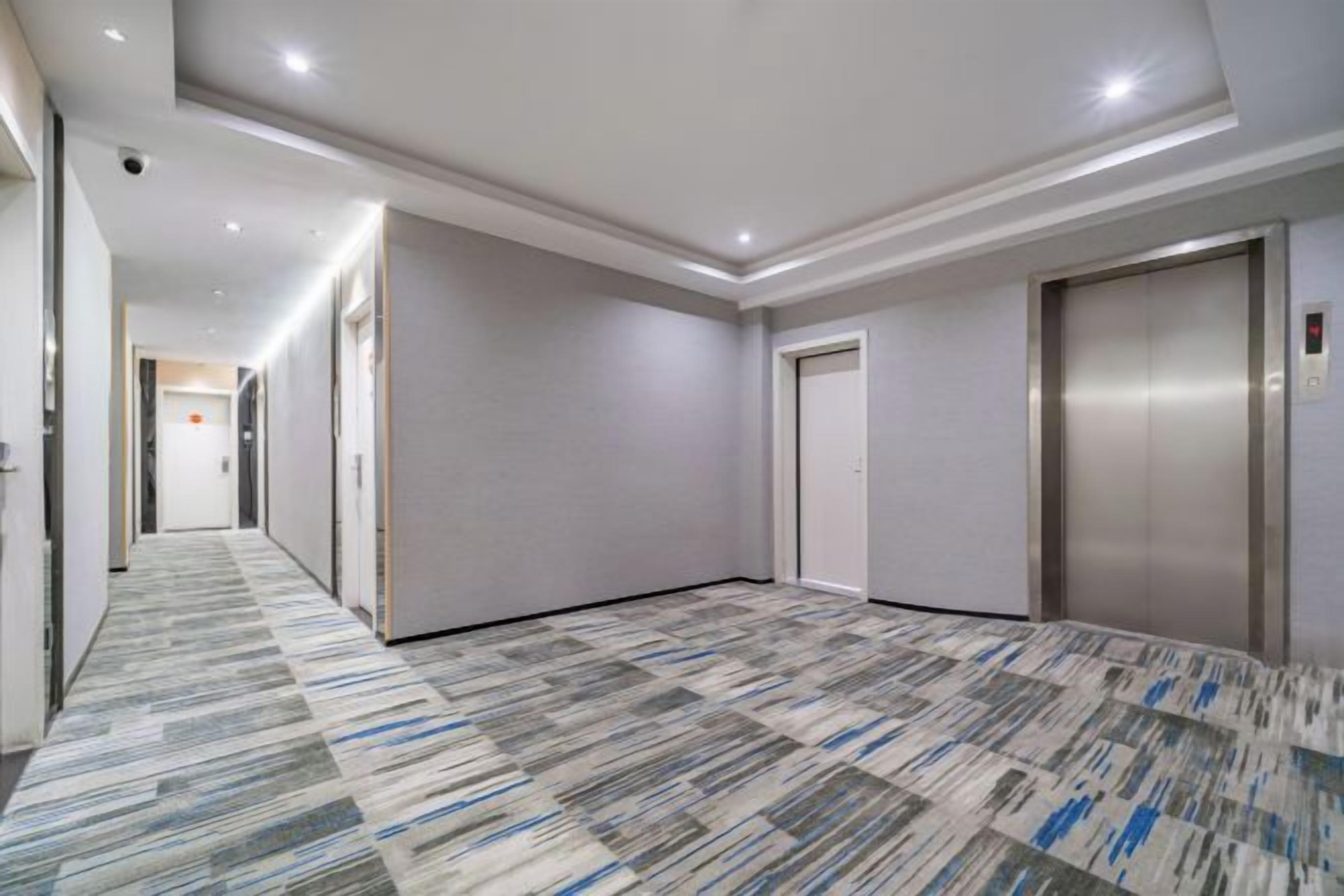 A hotel corridor with a patterned carpet, a door, and an elevator.