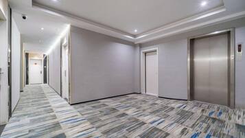 A hotel corridor with a patterned carpet, a door, and an elevator.