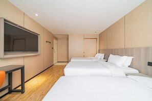 A hotel room with a large flat-screen TV, two beds, a desk, and a chair.