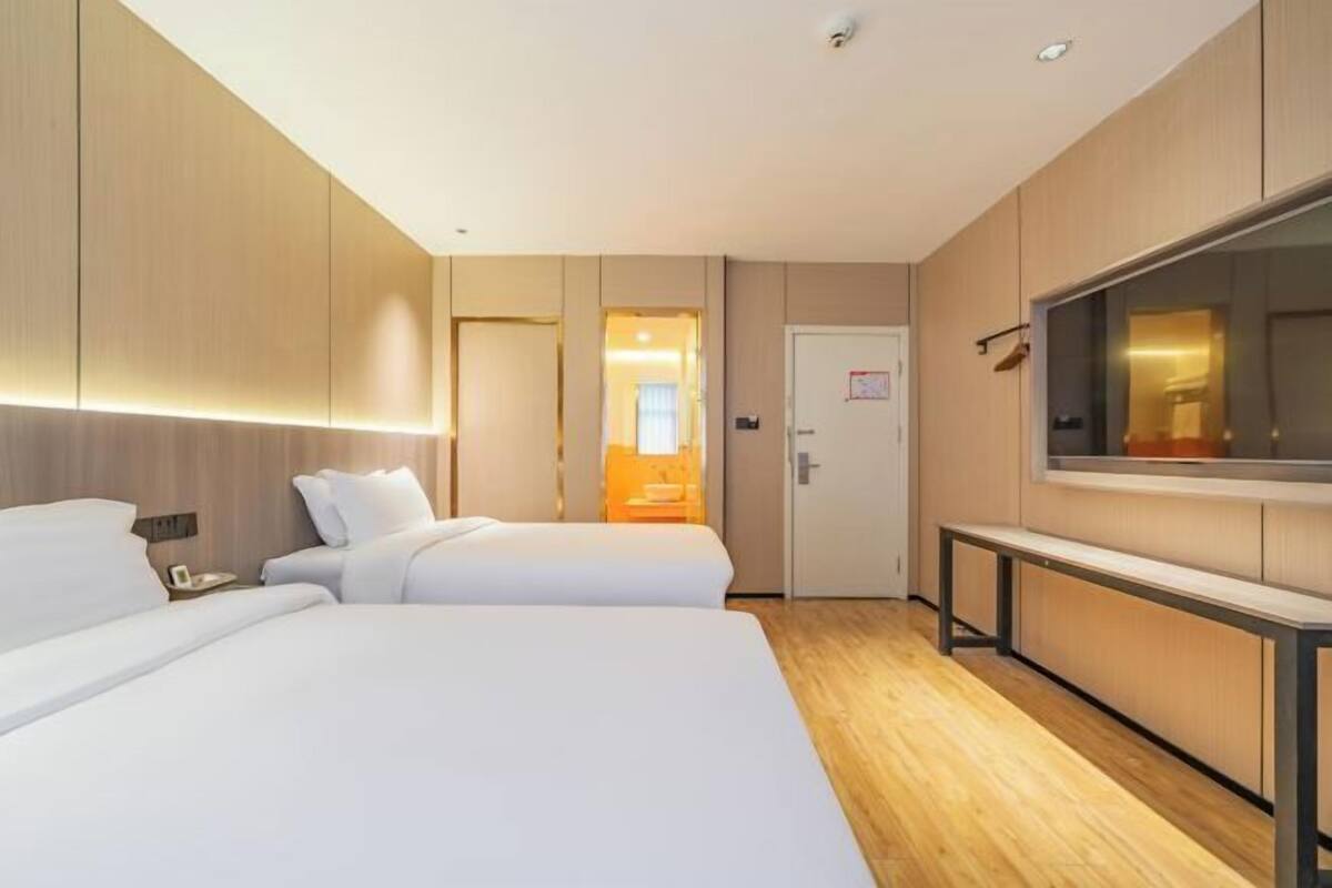Habitación de hotel con dos camas, televisor, escritorio y puerta que da a un baño.