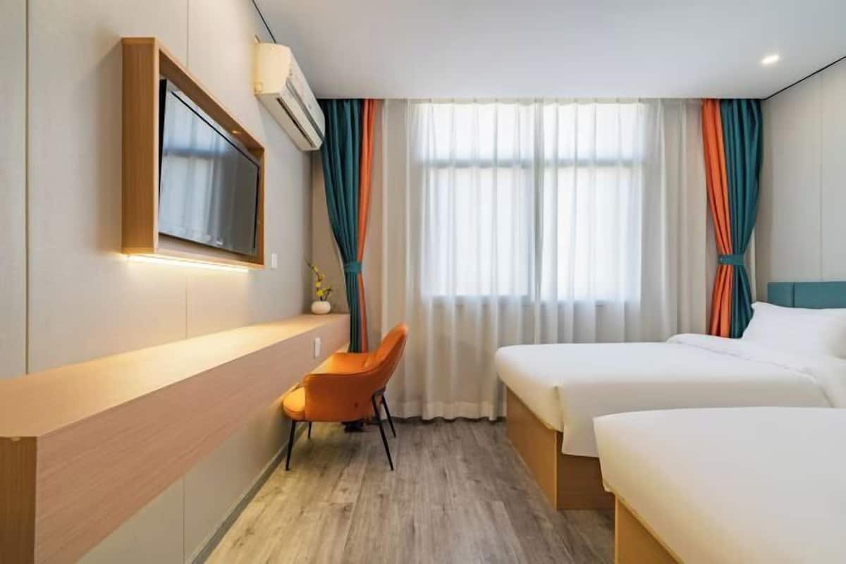 Una habitación de hotel con escritorio, dos camas, televisión y cortinas.