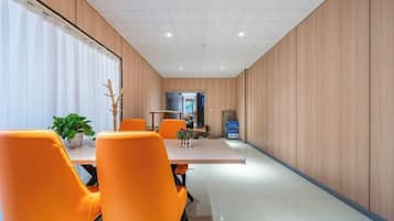 Une salle de réunion moderne, dotée d’une longue table et de chaises orange, de murs recouverts de panneaux en bois et d’un espace cuisine visible à l’arrière-plan.