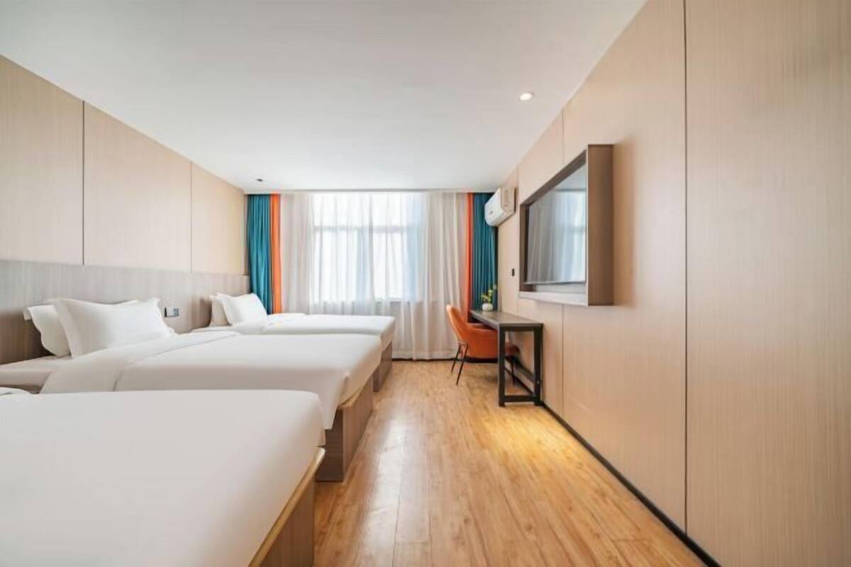 Habitación de hotel con tres camas, un escritorio, una silla y un ventanal con cortinas.