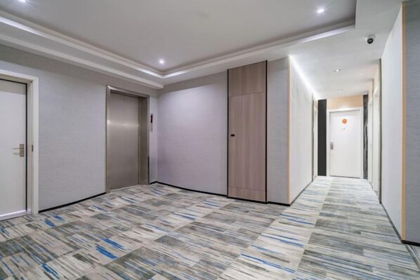 A hotel corridor with a patterned carpet, doors, and a light-colored wall.