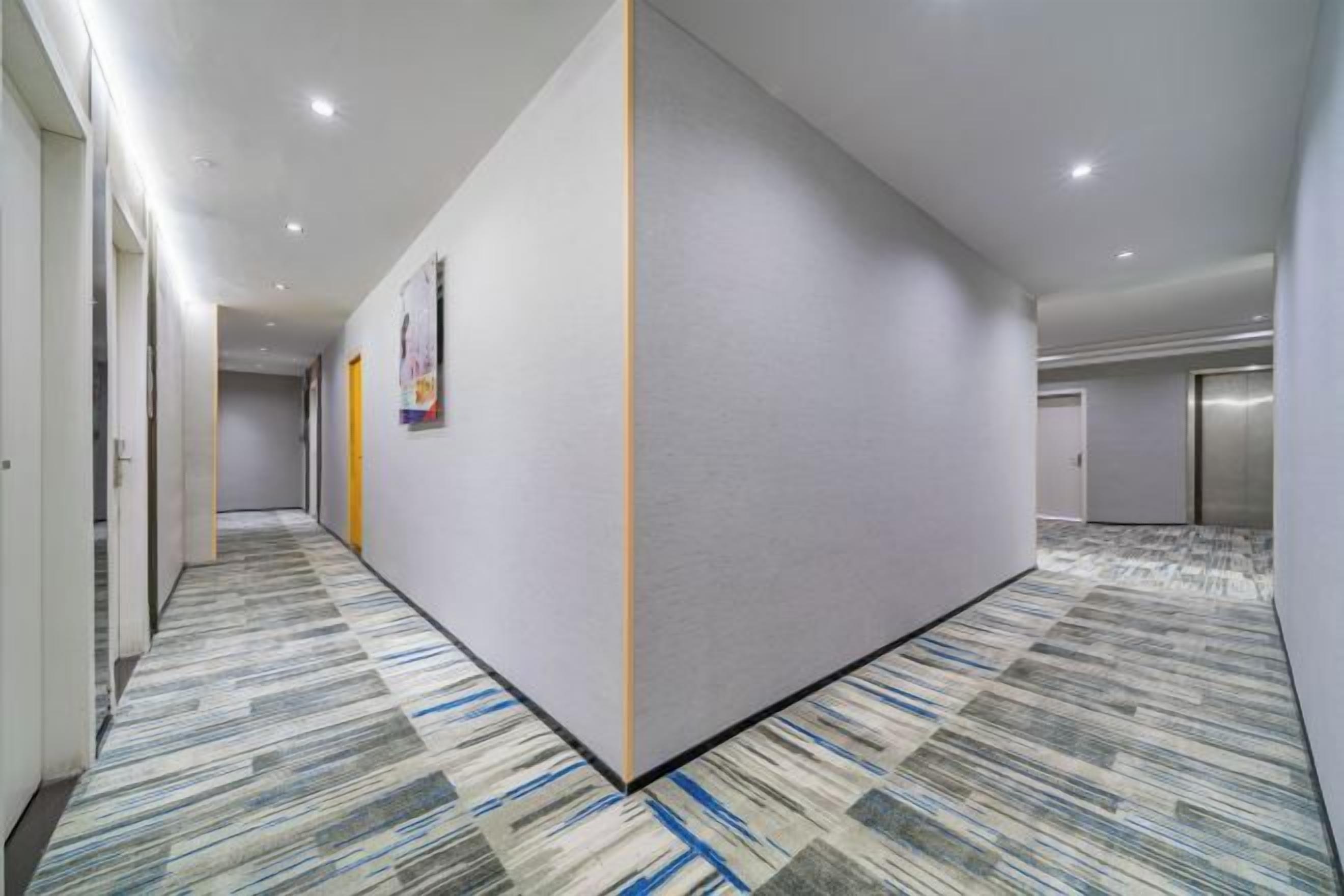 Un pasillo de hotel con alfombra estampada, un tabique y puertas que dan a las habitaciones.
