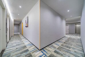 Un couloir d’hôtel avec un tapis à motifs, un mur de séparation et des portes donnant accès aux chambres.