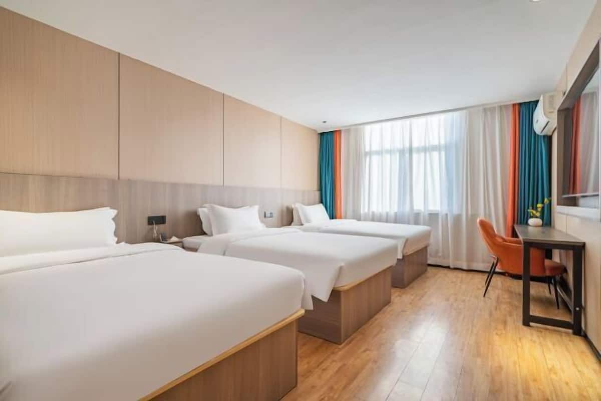 Habitación de hotel con tres camas, un escritorio y una silla.
