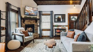 A cozy living room with a stone fireplace, a comfortable sofa, and a television mounted on the wall. - 2 King BRs-HotTub,Wifi,Pets,Mins to DT Sevierville (Sevierville)