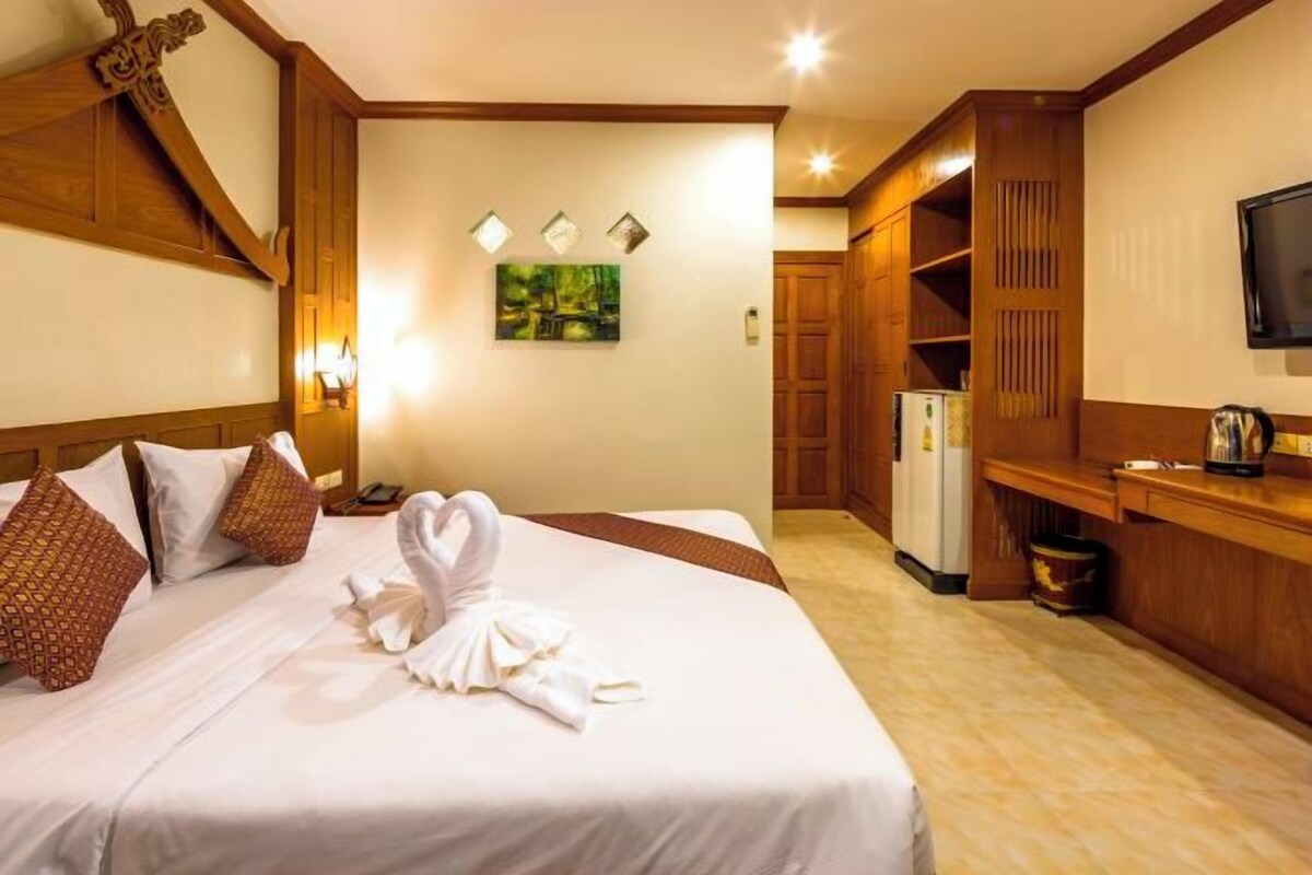 Una camera d'albergo con un letto rifatto, una testiera in legno, una TV a parete e un angolo cottura.